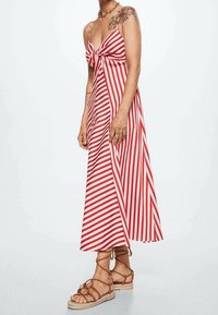 Robe maxi rayée rouge et blanche avec un devant noué, des bretelles spaghetti et une silhouette fluide. Associée à des sandales en cuir marron à lanières.