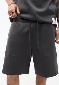 Donkergrijze katoenen shorts met elastische tailleband, trekkoord en twee voorzakken. Beschikt over een zachte textuur en eenvoudig ontwerp.