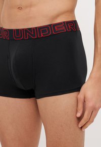 Schwarze Boxershorts mit taillierter Passform und rotem, markiertem Gummibund. Der Stoff wirkt glatt und hat minimale Nähte für zusätzlichen Komfort.