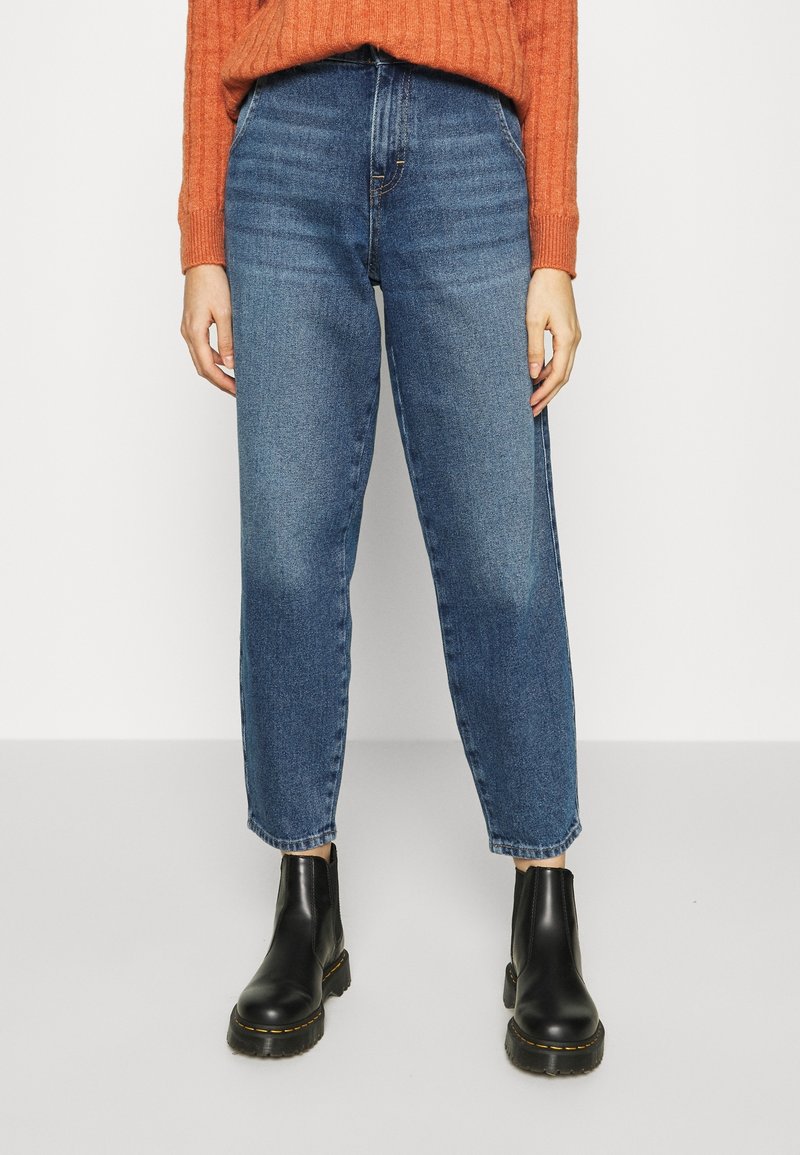 Jean en denim bleu avec une coupe droite, taille haute et décoloration minimale. Assorti à des bottines noires à semelle épaisse.