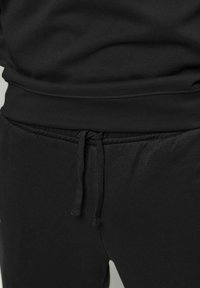 Nærbillede af sort joggingbukselinning med bundet snøre og matchende sort top, som er let stoppet ind.