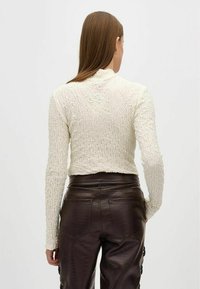Crème textuur top met lange mouwen en een cropped zoom, gecombineerd met donkerbruin nep lederen broek met zakken en een subtiel krokodillenpatroon.