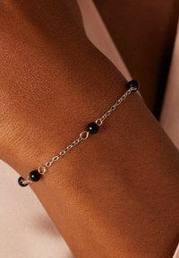 Silver chain bracelet with alternating black beads, featuring a delicate design. The bracelet is worn on a textured skin surface.