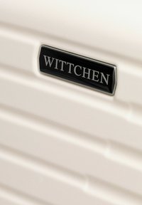 Biała walizka o teksturowanej powierzchni; posiada rowki oraz czarną metalową metkę z napisem "WITTCHEN." Gładkie wykończenie i elegancki design.