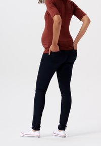 Mörkblå skinny jeans med en slät yta, med bakfickor, tillsammans med en figurnära, rostfärgad topp och vita sneakers.