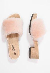 Dřevěné platformové sandály s měkkým, růžovým kožíškem. Základna je z lehkého dřeva s konturovaným designem a gumovou podrážkou pro lepší přilnavost.