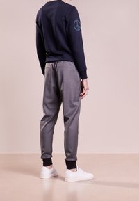 Granatowy sweter z haftem symbolem pokoju na rękawie, w połączeniu z szarymi zwężanymi spodniami i białymi trampkami z czarnymi akcentami.
