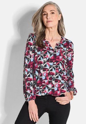 Mehrfarbige Bluse mit einem geometrischen Muster in Pink, Rot, Schwarz und Blau. Hergestellt aus leichtem Material mit V-Ausschnitt und elastischen Ärmeln.
