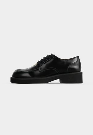 Chaussure de ville en cuir noir avec un laçage à l’avant, un bout arrondi, un talon bas et des détails cousus sur les côtés.