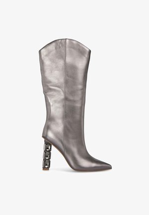 Botte argentée métallisée montante avec un bout pointu et un talon géométrique épais comportant des accents noirs. Texture lisse et design épuré.