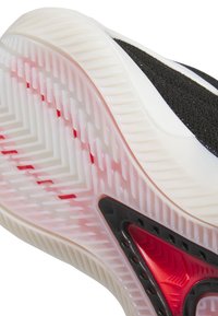 Lähikuva tennarin pohjasta, jossa näkyy läpikuultava valkoinen pito-osa, jossa on punaisia korostuksia sekä musta-punainen kolmiomainen tukielementti.