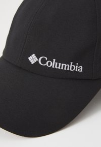Czarna czapka z tkaniny, z wyginanym daszkiem i białym logo "Columbia" na przedniej części, z widocznymi detalami haftu.