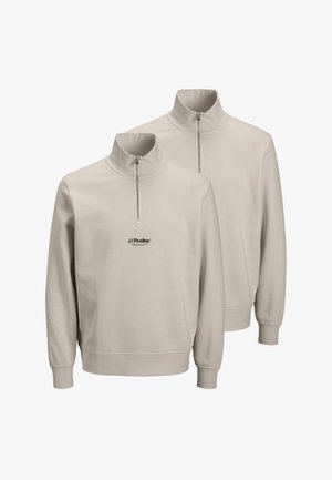 Beige Halbreissverschluss-Sweatshirts mit hohen Kragen und gerippten Bündchen, ausgestattet mit einem kleinen schwarzen "JJ Studios"-Logo auf der Vorderseite. Zwei Sweatshirts abgebildet.