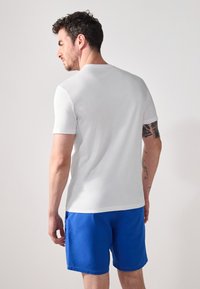 White short-sleeve t-shirt with a crew neckline, paired with blue shorts. The fabric appears smooth with a regular fit.