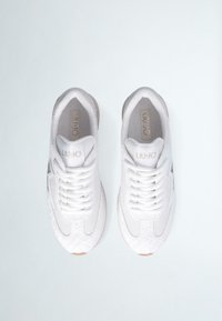 Scarpe sportive bianche con tomaia in rete, accenti testurizzati e lacci piatti. Presentano una suola in gomma marrone chiaro e un dettaglio di branding metallico.