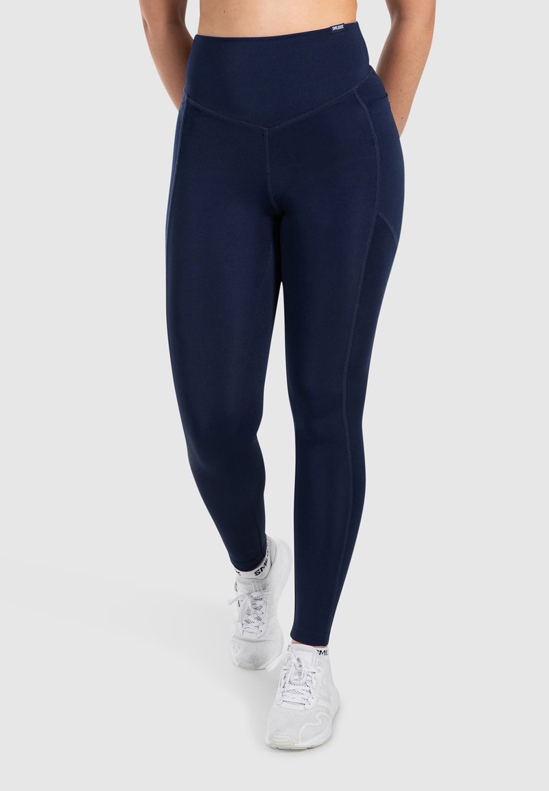 Leggings alta in vita di colore navy, realizzati in tessuto elastico con una texture liscia. Presentano dettagli delle cuciture e una silhouette aderente. Indossati con sneakers bianche.