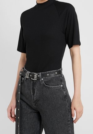 Person iført en sort ribbet kortærmet top, der er stoppet ned i højttaljede, falmede sorte jeans med et dekorativt sort bælte.