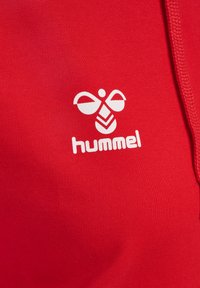 Roter Stoff mit glatter Textur, auf dem ein weißes Logo eines stilisierten Insekts und darunter das Wort "hummel" abgebildet sind.