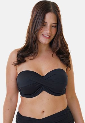 Woman with long brown hair wearing a black strapless bikini top and matching bottom, smiling with eyes looking down.