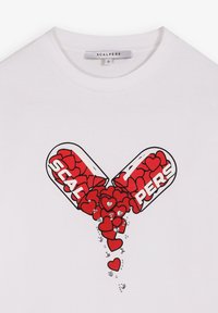 Witte T-shirt met een afbeelding van een capsule die open is gesplijt en rode en zilveren hartvormen uitstort, en het woord "SCALPERS" binnen de capsule.