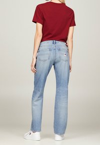 Jeans de pierna recta en azul claro, con un acabado descolorido, dos bolsillos traseros y una etiqueta tejida cerca de la cintura. Combinados con una camiseta de color burdeos.