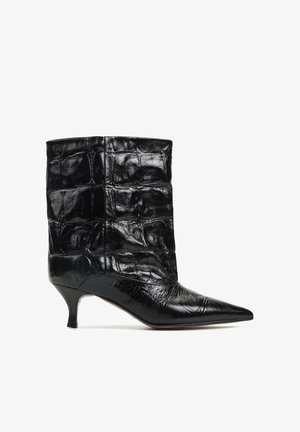 Czarny skórzany botek sięgający do połowy łydki z teksturą przypominającą skórę krokodyla, zaostrzonym noskiem i niskim kocim obcasem, pokazany na białym tle.