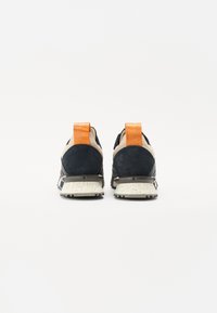 Námořnické modré sportovní boty s svrchní částí z semiše a síťoviny, oranžovým poutkem na patě a skvrnitou bílou podrážkou. Pohled ze dvou stran na bílém pozadí.