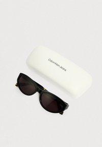 Czarne okulary przeciwsłoneczne z ciemnymi soczewkami, o smukłym designie. W zestawie białe etui Calvin Klein Jeans z wytłoczonym logo.