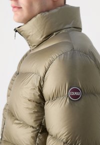 Padded olive green jacket made from shiny material, featuring a high collar and a round logo patch with "COLMAR" on the sleeve.