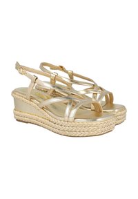 Sandalias de cuña doradas con un brillo metálico, que cuentan con tiras entrecruzadas, una hebilla en el tobillo y una suela de plataforma de yute trenzado.