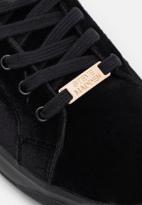 Černé sametové tenisky s výraznými tkaničkami, elegantním designem a zlatou kovovou visačkou s vyraženým nápisem "STEVE MADDEN." Viditelná gumová podrážka.