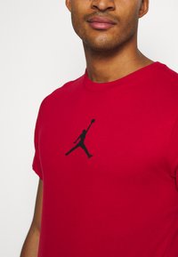 Rød bomulds T-shirt med et sort silhuetlogo på brystet. Korte ærmer og rund halsudskæring. Blød tekstur med et afslappet design.