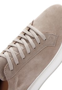 Sneaker in suede beige chiaro con lacci abbinati, caratterizzato da una texture liscia, cuciture minime e una suola in gomma bianca.
