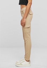 Béžové cargo nohavice so slim fit strihom, vybavené bočnými vreckami a hladkou textúrou. V kombinácii s bielymi teniskami a skráteným čiernym topom.