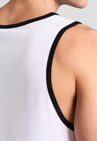 Canotta bianca in rete con bordi neri, caratterizzata da una texture traspirante e un design racerback che espone parte della parte superiore della schiena e della spalla.
