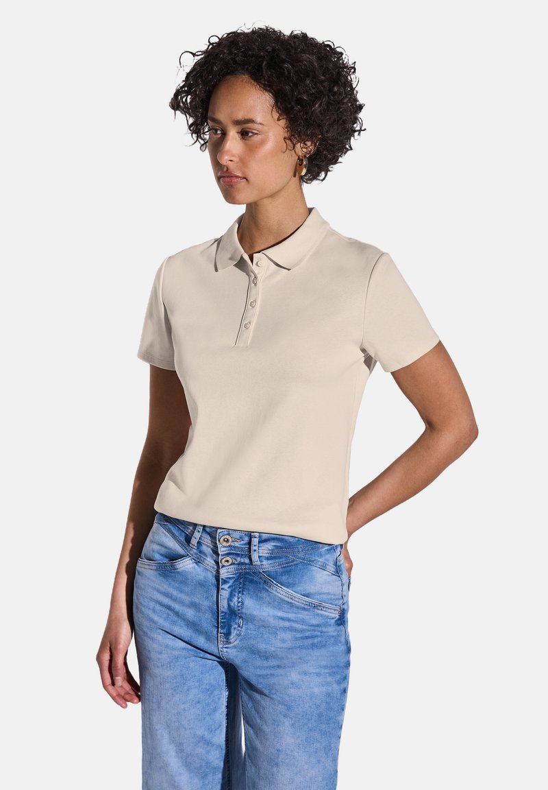 Beige kortärmad polotröja med klassisk krage och tre knappar, tillsammans med ljusblå denimjeans med fem fickor.
