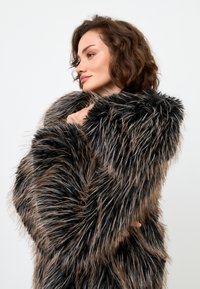 Palton din blană artificială negru și maro, cu o textură lungă și cârlionțată, având un guler lat și o croială lejeră, care se lasă pe umăr.