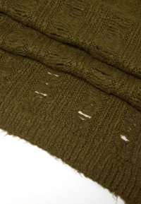 Coperta lavorata a maglia verde oliva, con texture a moduli rialzati e sezioni a rete. Materiale morbido in lana con bordi sfilacciati.