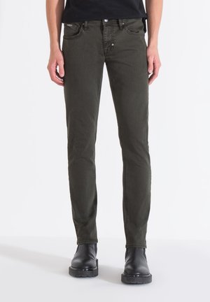 Jeans de corte slim en verde oscuro, fabricados en una mezcla de algodón, con cinco bolsillos, herrajes de remache y un cierre clásico de botón. Textura suave.