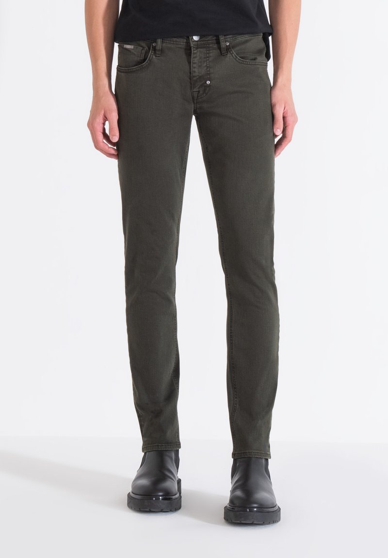 Jeans de corte slim en verde oscuro, fabricados en una mezcla de algodón, con cinco bolsillos, herrajes de remache y un cierre clásico de botón. Textura suave.