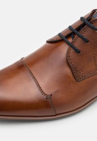 Chaussure habillée en cuir marron avec panneau latéral texturé, lacets noirs et couture détaillée sur fond blanc.