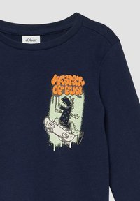 Granatowa koszulka z rysunkowym dinozaurem jeżdżącym na desce skateboardowej oraz pomarańczowym napisem "Mistrz Zabawy" powyżej.
