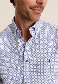 Blauwe en witte gebloemde button-up shirt met een bloemenpatroon, puntige kraag en blauwe knopen. Gemaakt van lichtgewicht katoen.