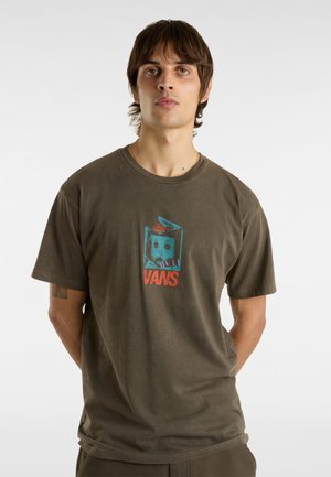 Olivgrön bomulls-t-shirt med rund hals, som har en färgglad grafisk tryck av ett ansikte och texten "VANS" i mitten. Kort ärm.