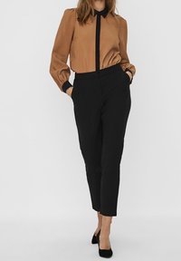 Blusa beige con maniche a sbuffo e colletto nero, abbinata a pantaloni neri slim-fit. Le scarpe sono tacchi a punta neri.