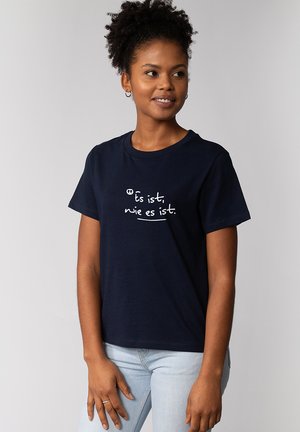 T-shirt en coton bleu marine à manches courtes, avec un texte imprimé en blanc en cursive : « Es ist, wie es ist. » sur le devant.