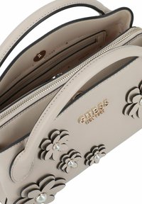 Beige Handtasche aus Kunstleder mit künstlichen Blumenakzenten, goldfarbenem Logo, Reißverschluss und zwei Tragegriffen. Das Innere verfügt über Kartenfächer.
