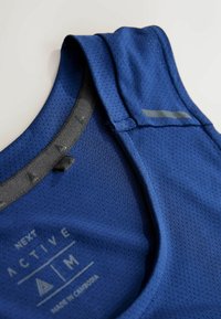 Niebieski sportowy top na ramiączkach z teksturowanej, oddychającej tkaniny. Posiada szare wykończenie wokół dekoltu oraz nadrukowaną etykietę marki wewnątrz.