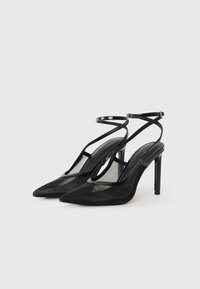 Chaussures à talons hauts en cuir verni noir avec un bout pointu, des panneaux en filet transparent et une sangle de cheville dotée d'une fermeture à boucle.