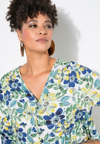 Blusa con stampa floreale su sfondo bianco, caratterizzata da fiori blu, gialli e verdi. Vestibilità ampia con scollatura a V e dettagli in bottone.